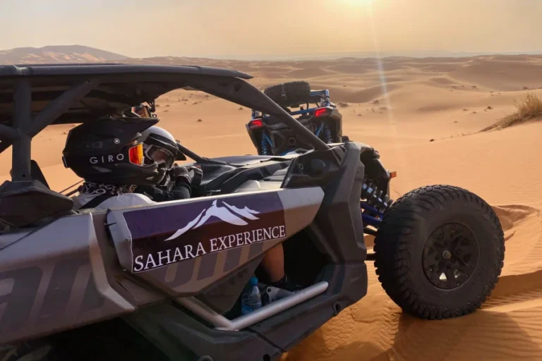 Dos buggies con la marca "Sahara Experience" atraviesan las dunas del desierto bajo un cielo brumoso.